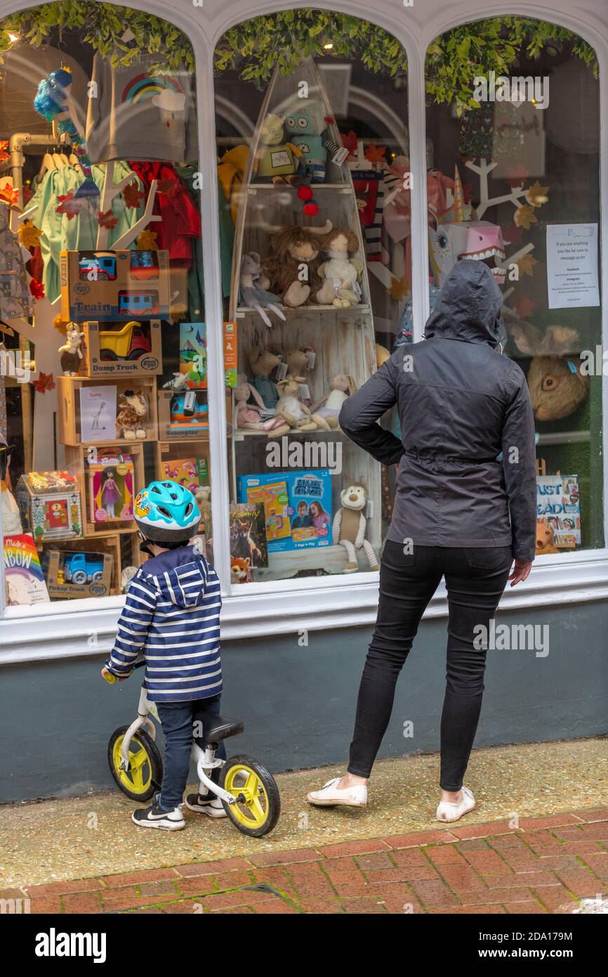 una giovane donna e un piccolo bambino che cavalcano una bicicletta guardando in una vetrina dei giocattoli in una giornata piovosa. Foto Stock