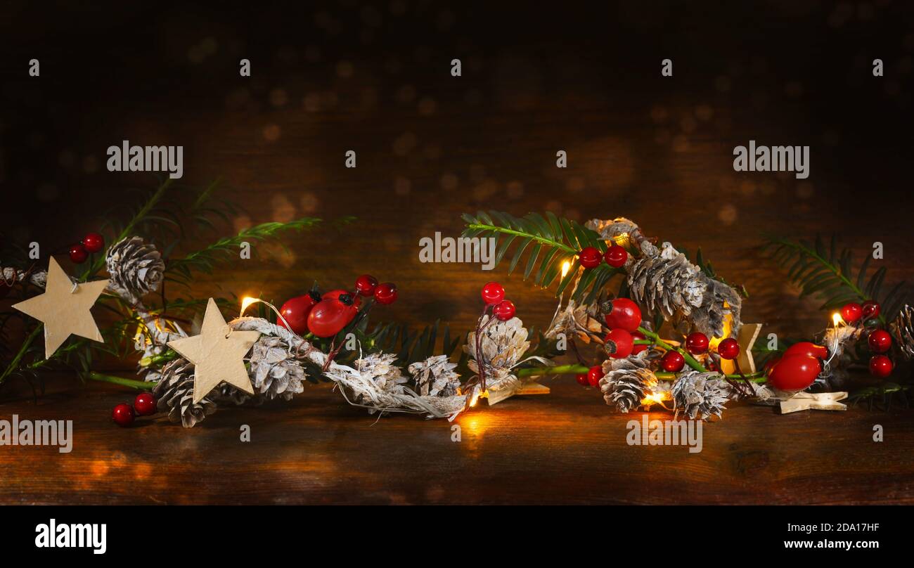 Decorazione di Natale con rami, coni, fianchi di rose, stelle e luci calde su uno sfondo di legno scuro, spazio di copia Foto Stock
