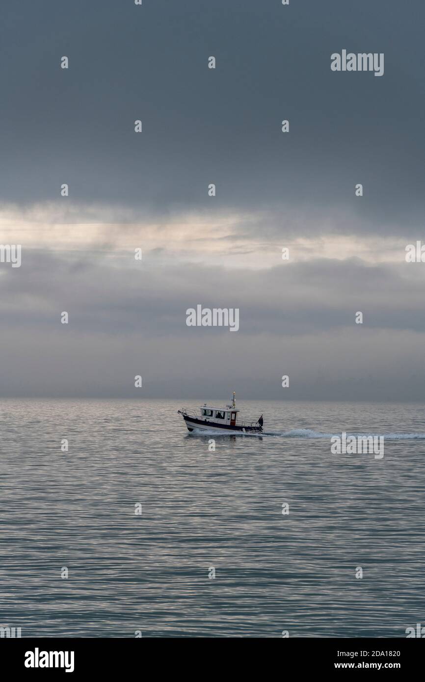 una piccola barca da pesca sotto un grande cielo scuro tempestoso in direzione di casa prima di una tempesta. Foto Stock