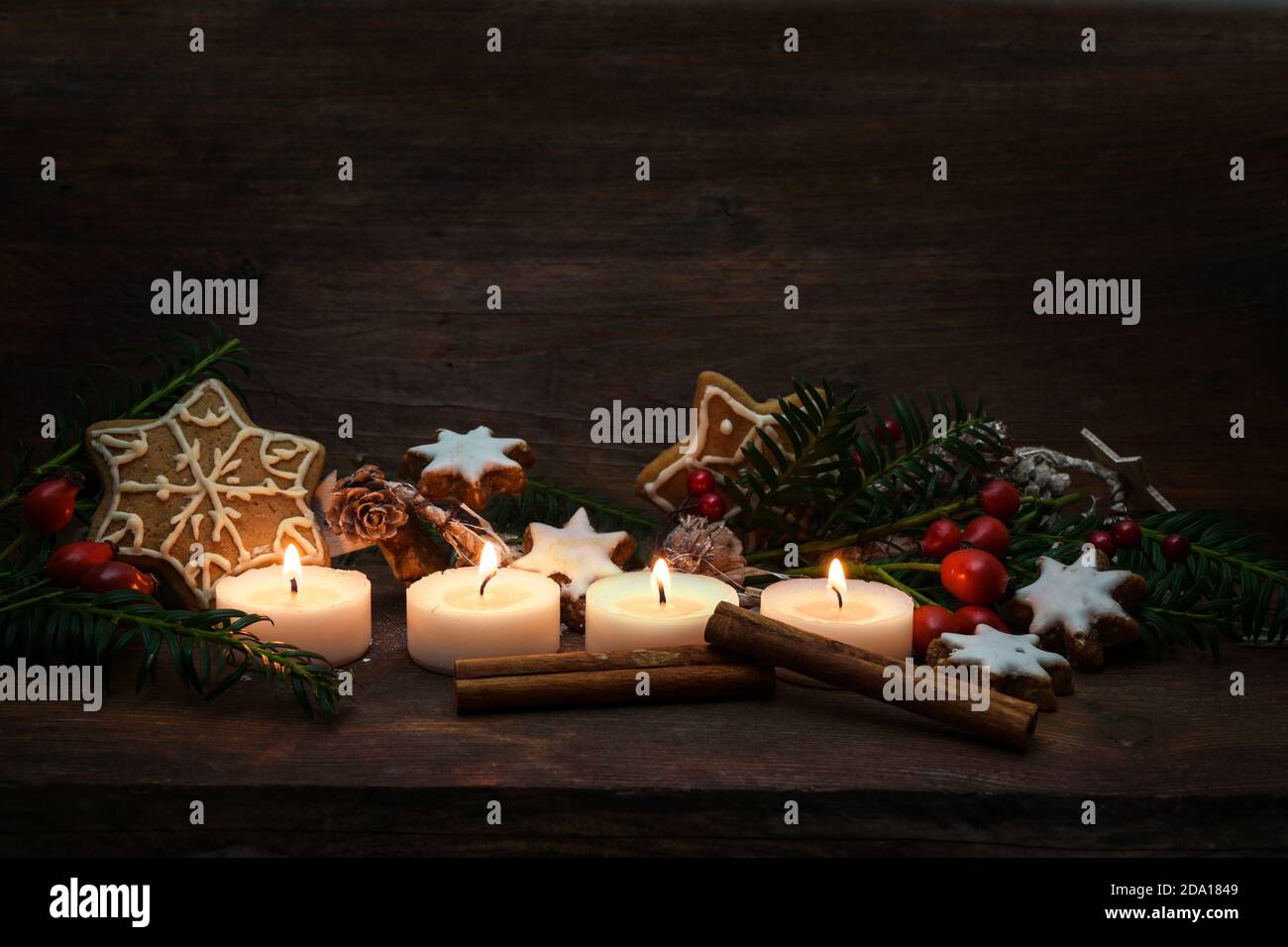 Quattro piccole candele illuminate per l'Avvento e la decorazione di Natale come biscotti di pan di zenzero, rami e fianchi di rosa su uno sfondo di legno rustico scuro, genere Foto Stock