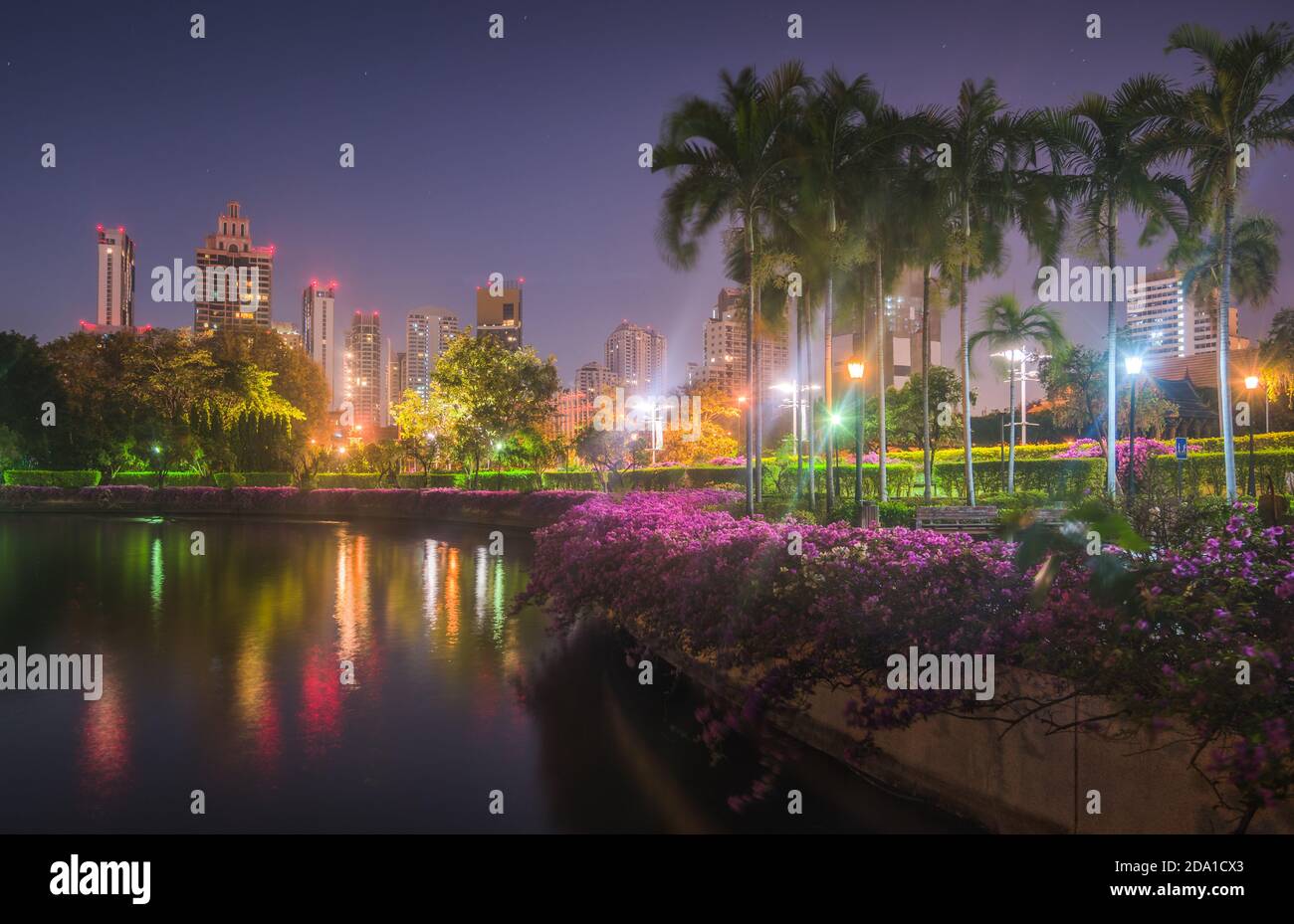 Lago con acqua calma che riflette edifici vicini nella parte sud del Parco pubblico Benjakiti di notte a Bangkok, Thailandia Foto Stock