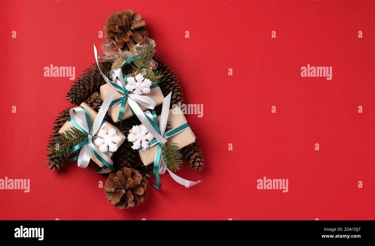 Albero di Natale alternativo fatto di regali e coni di albero su un rosso. Spazio per i desideri. Tessera vacanze. Vista dall'alto. Felice Anno Nuovo. Foto Stock