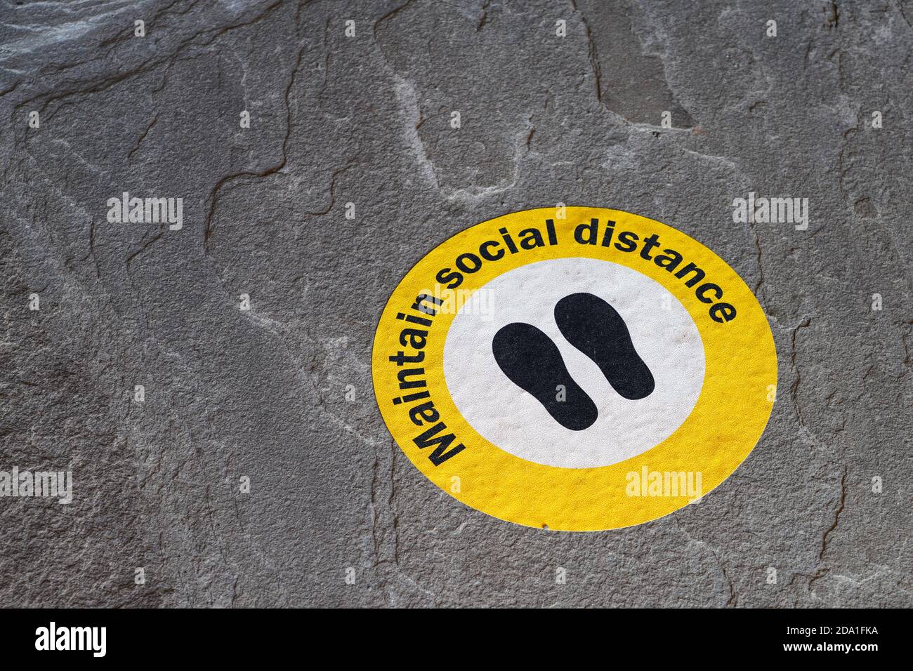 Vista di un segno giallo che dice mantenere la distanza sociale su Il terreno durante la pandemia del Covid-19 del 2020 Foto Stock