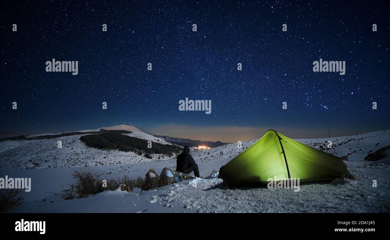 Notte stellata sull'uomo guardando il paesaggio invernale del Parco dei Nebrodi da una tenda luminosa, Sicilia Foto Stock