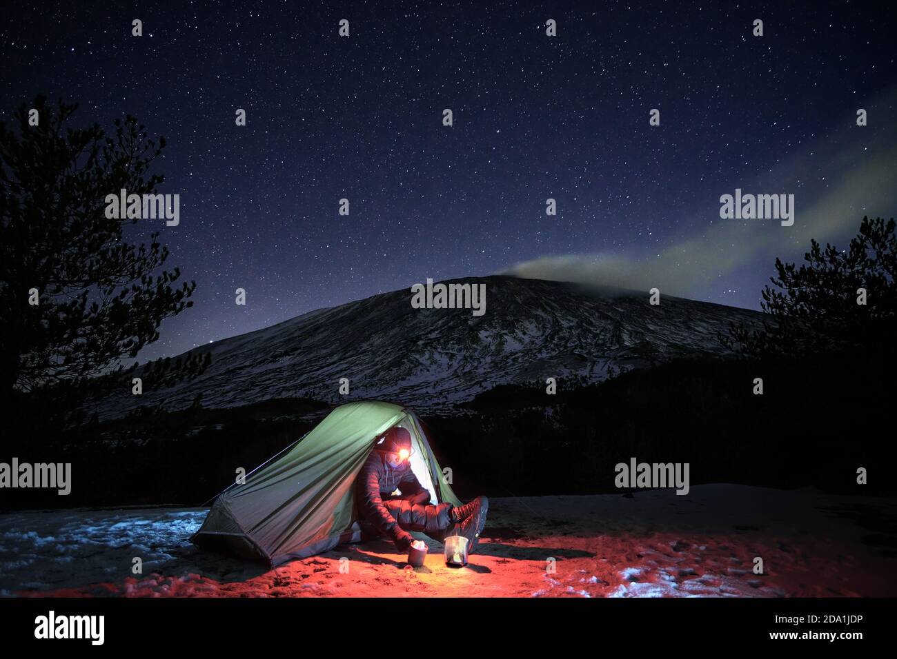 Uomo che riposa nella sua tenda illuminata sulla neve sotto cielo stellato, sullo sfondo Etna Monte, Sicilia Foto Stock