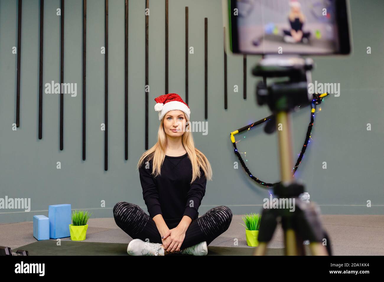 Attraente blogger donna a Santa Hat in sportswear record esercizi per l'allenamento per il suo vlog. Blogging. Stile di vita sano e sportivo. Foto Stock