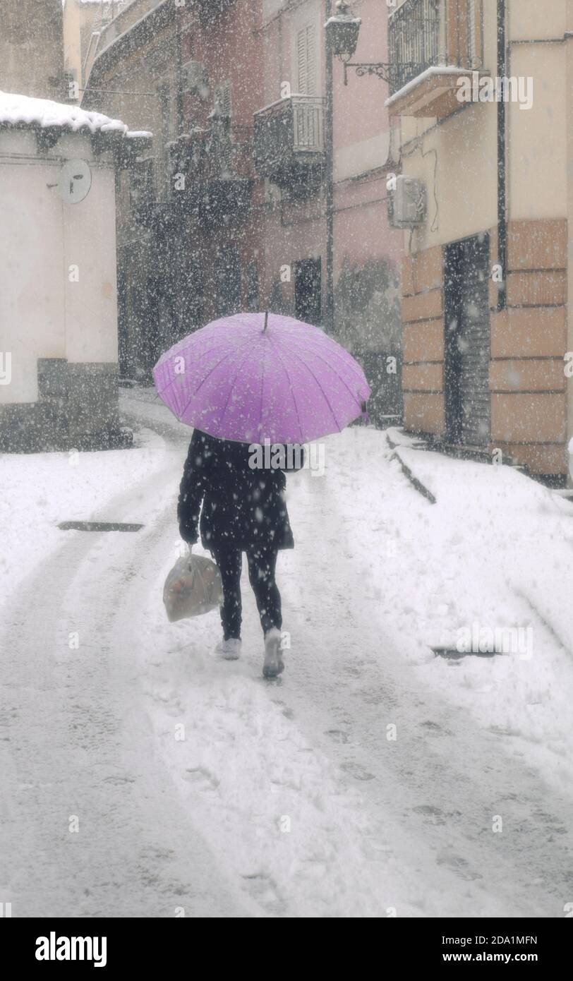 una donna che cammina attraverso la neve con un ombrello lilla Foto Stock