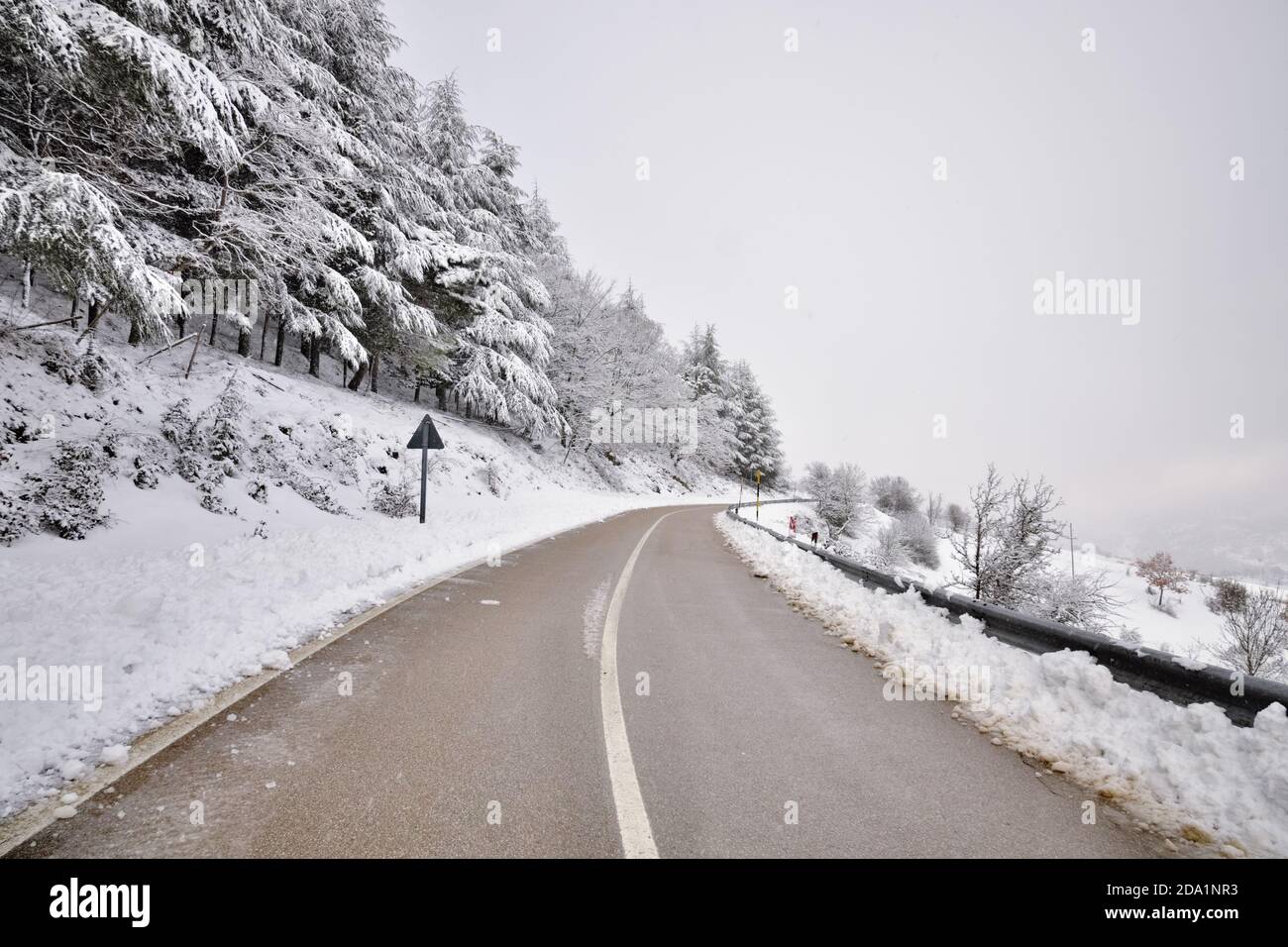 La strada di montagna curva attraversa la foresta innevata fino al Parco Nazionale dei Nebrodi in Sicilia, Italia Foto Stock