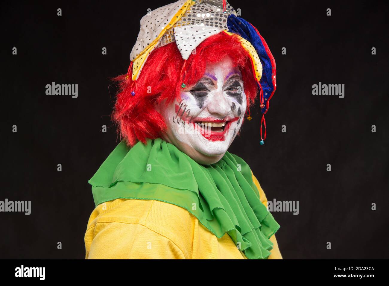 Un orribile clown con un terribile per il make-up e hat sulla sua testa ridere su uno sfondo nero Foto Stock