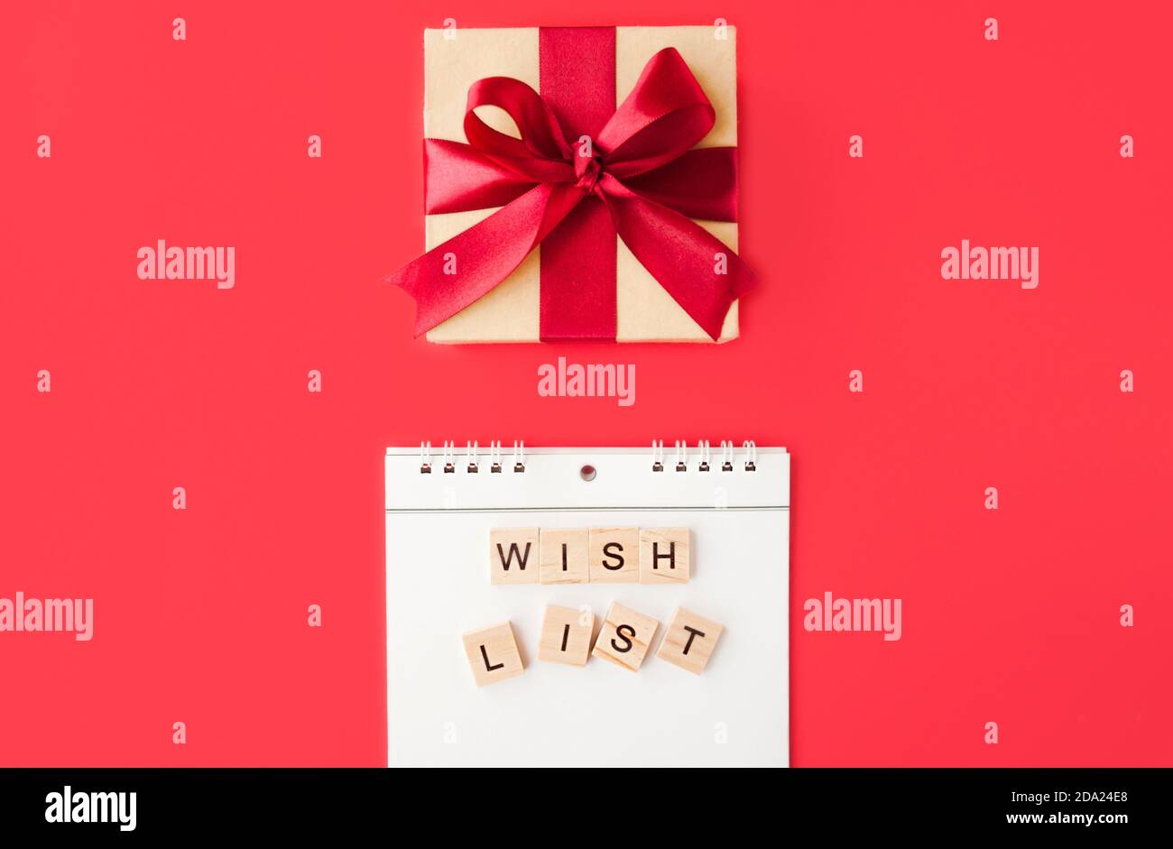 Quaderno a spirale bianco e wishlist quadrata su sfondo rosso, confezione regalo in carta Kraft con arco in raso rosso, fuoco selettivo Foto Stock