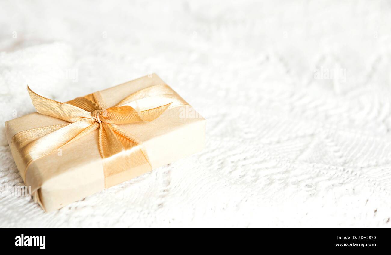 Scatola con regalo di Natale in carta chiara è legata con un nastro d'oro su sfondo bianco lavorato a maglia con decorazione. Golden ghirland di stelle. Anno nuovo. Congratul Foto Stock