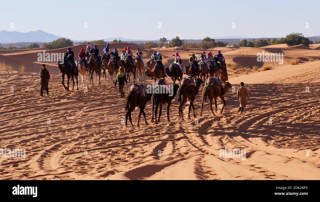 Merzouga, Marocco - 12/30/2019: I turisti che si godono un giro in cammello dromedario nelle dune di sabbia di Erg Chebbi, una popolare destinazione turistica. Foto Stock