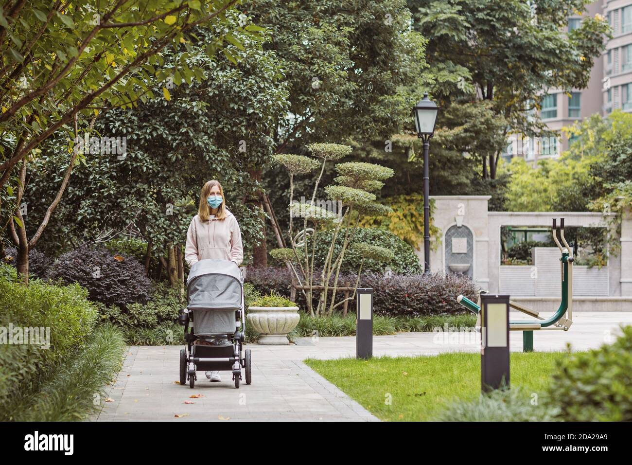 giovane madre caucasica che cammina con il neonato in buggy a causa del coronavirus covid-19 blocco pandemico. Persone che indossano maschera per la malattia Foto Stock