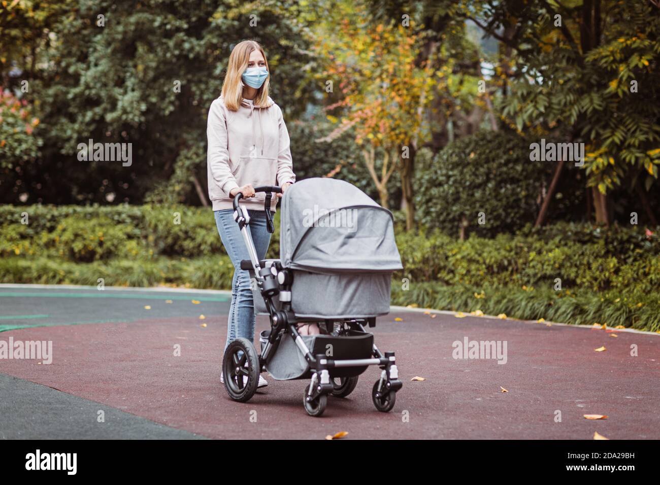 giovane madre caucasica che cammina con il neonato in buggy a causa del coronavirus covid-19 blocco pandemico. Persone che indossano maschera per la malattia Foto Stock
