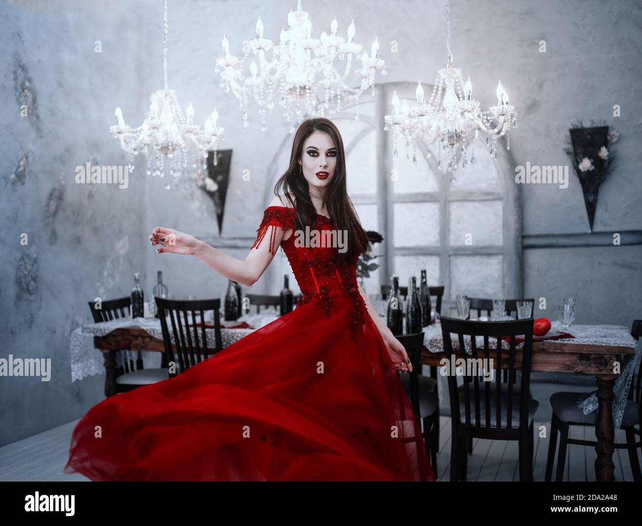 Vampiro femminile assetato di sangue in abito rosso. Interni medievali Foto Stock