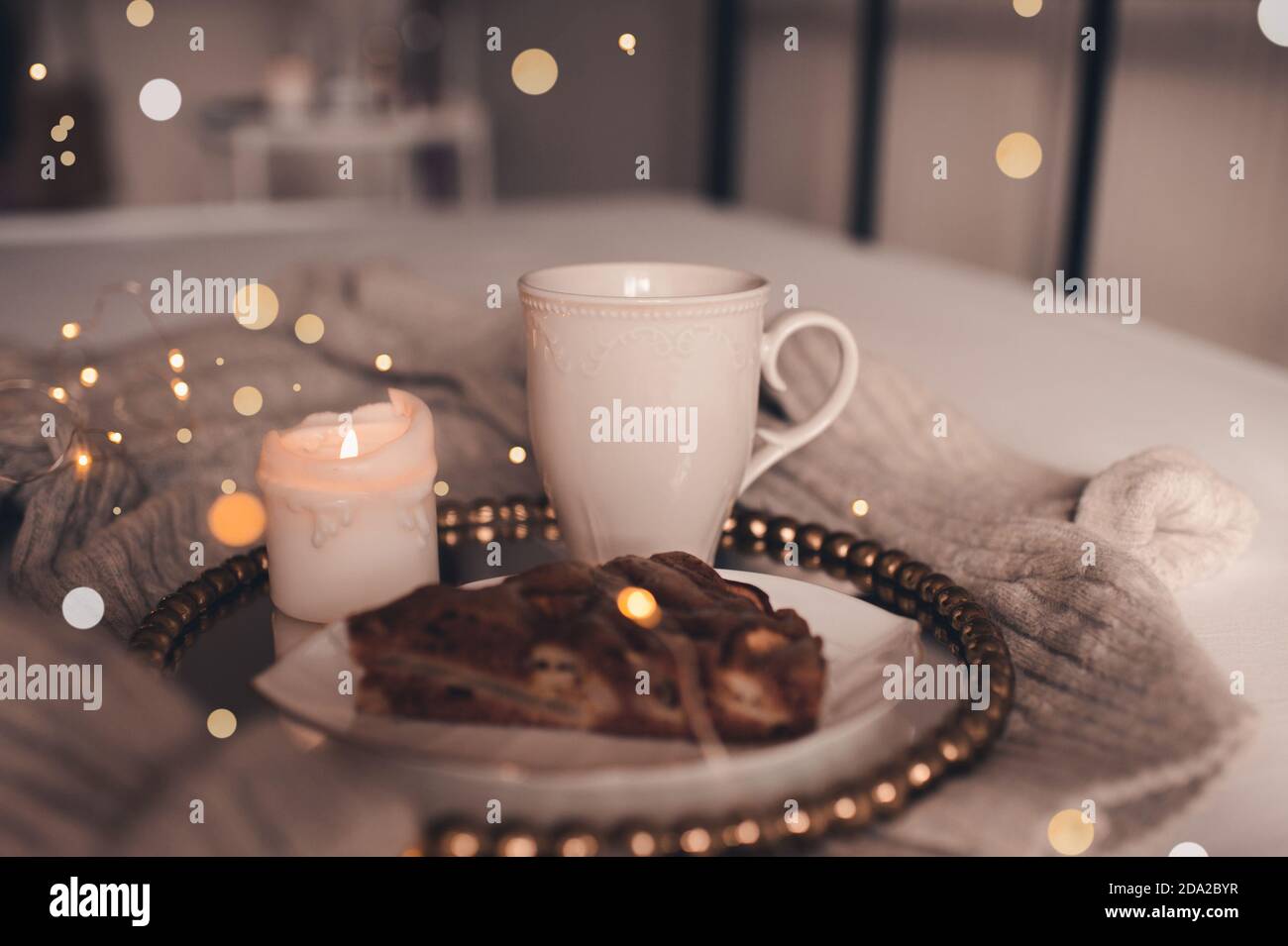 Tazza di caffè con candela bruciante e torta di cioccolato a letto sopra le luci di Natale primo piano. Buongiorno. Stagione invernale. Foto Stock