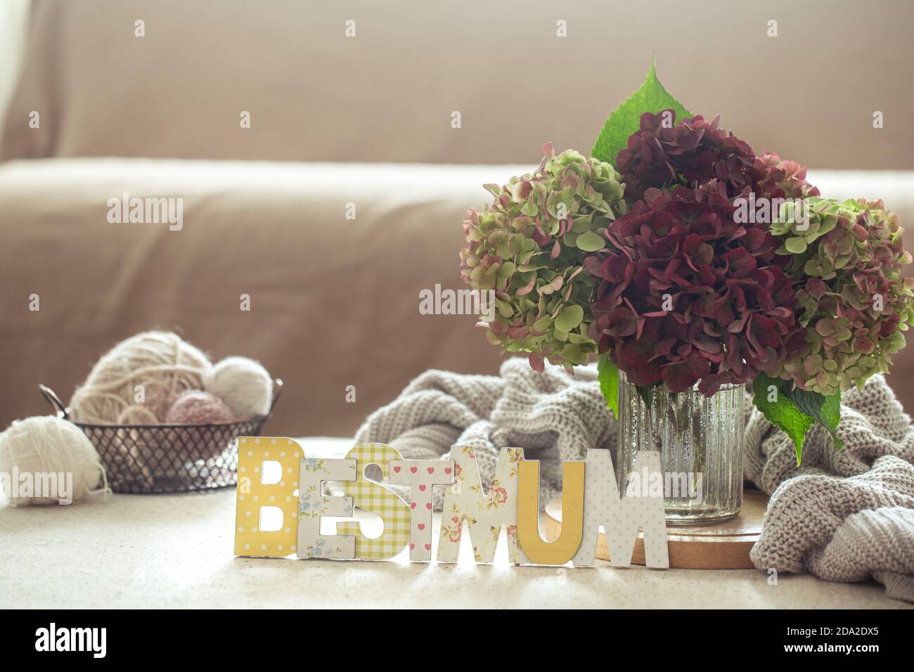 Ancora vita di fiori di idrangea in un vaso di vetro, maglioni, fili e decorazione la migliore mamma in primo piano. Foto Stock