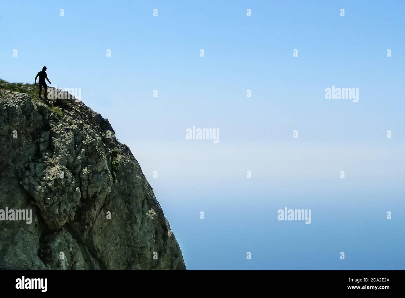 Un uomo su una roccia vicino al bordo dell'abisso. Una scogliera contro un cielo blu e un uomo che può cadere. Rischio, paura e vicinanza della morte. Un passo per l'i Foto Stock