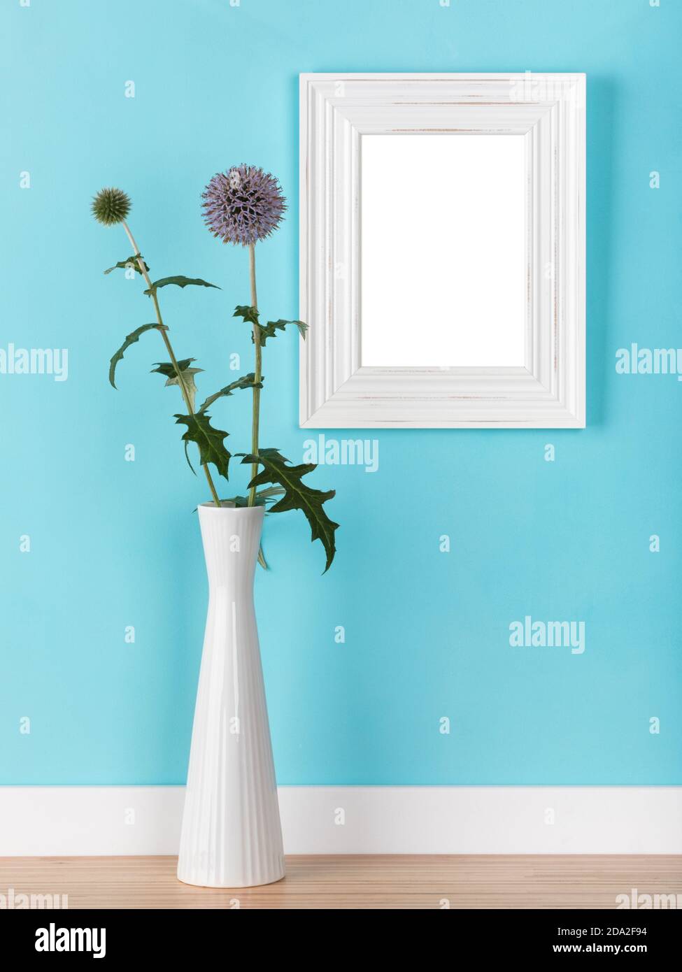 Mockup verticale con cornice bianca in shabby, modello con thistles globo in vaso davanti alla parete blu chiaro. Area immagine vuota mascherata con tracciato di ritaglio Foto Stock