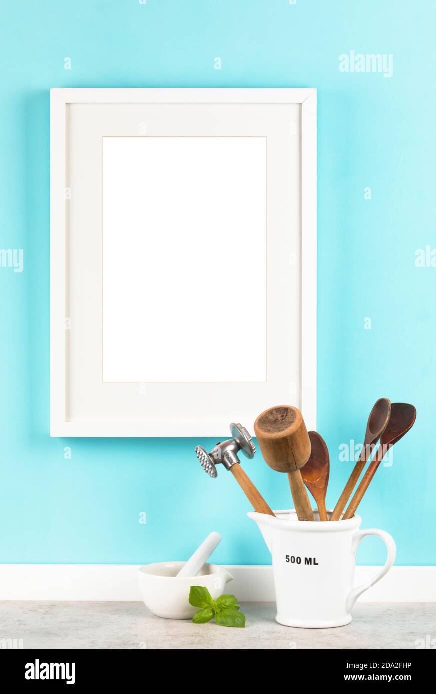 Cornice verticale bianca con formato 2x3 opaco su mockup blu da cucina. Misurino con utensili da cucina e mortaio con basilico lasciare Foto Stock
