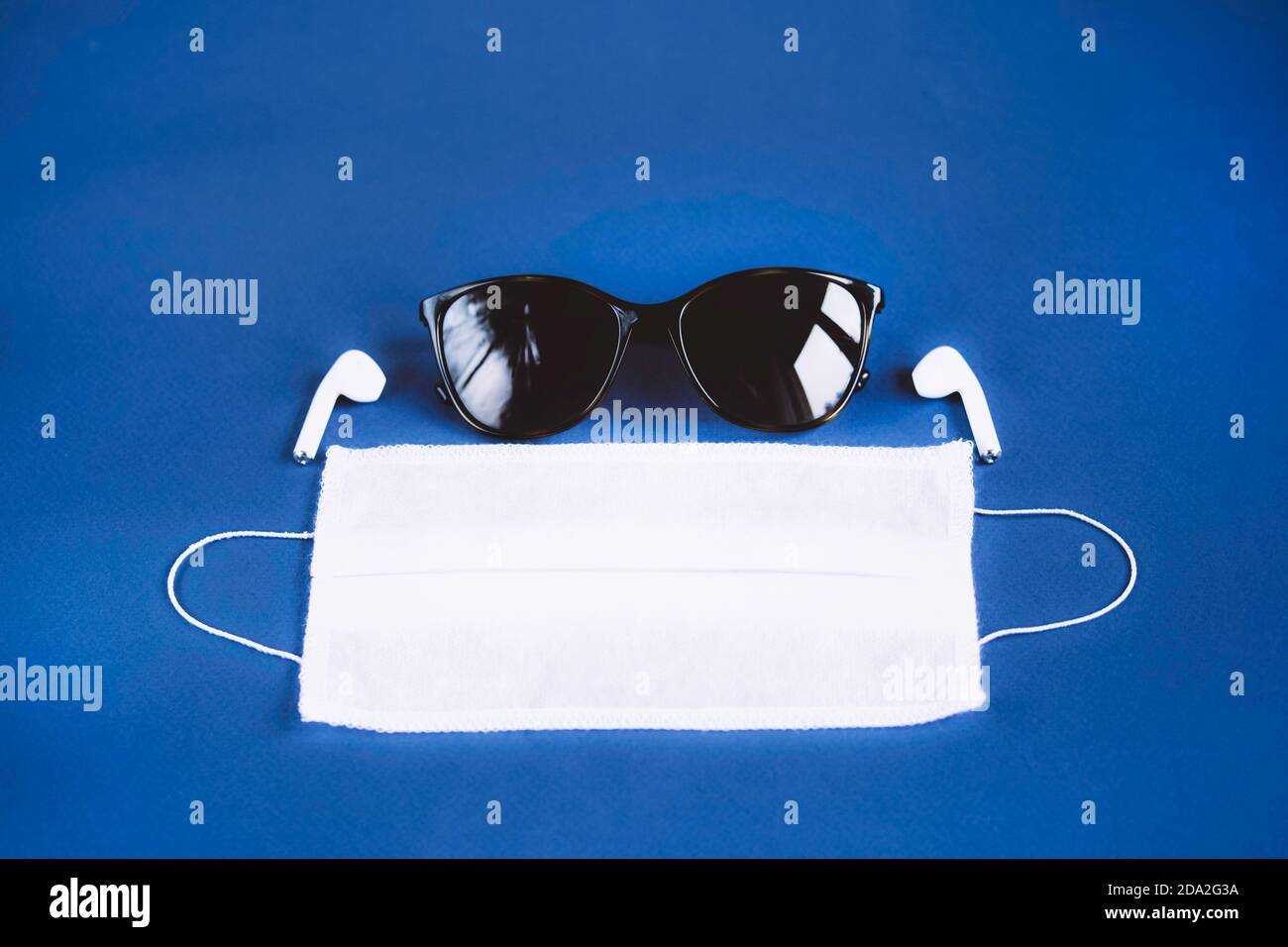 Accessori essenziali per la persona moderna su sfondo blu scuro. Occhiali da sole, maschera medica e cuffie wireless. Tendenze 2020. Foto Stock
