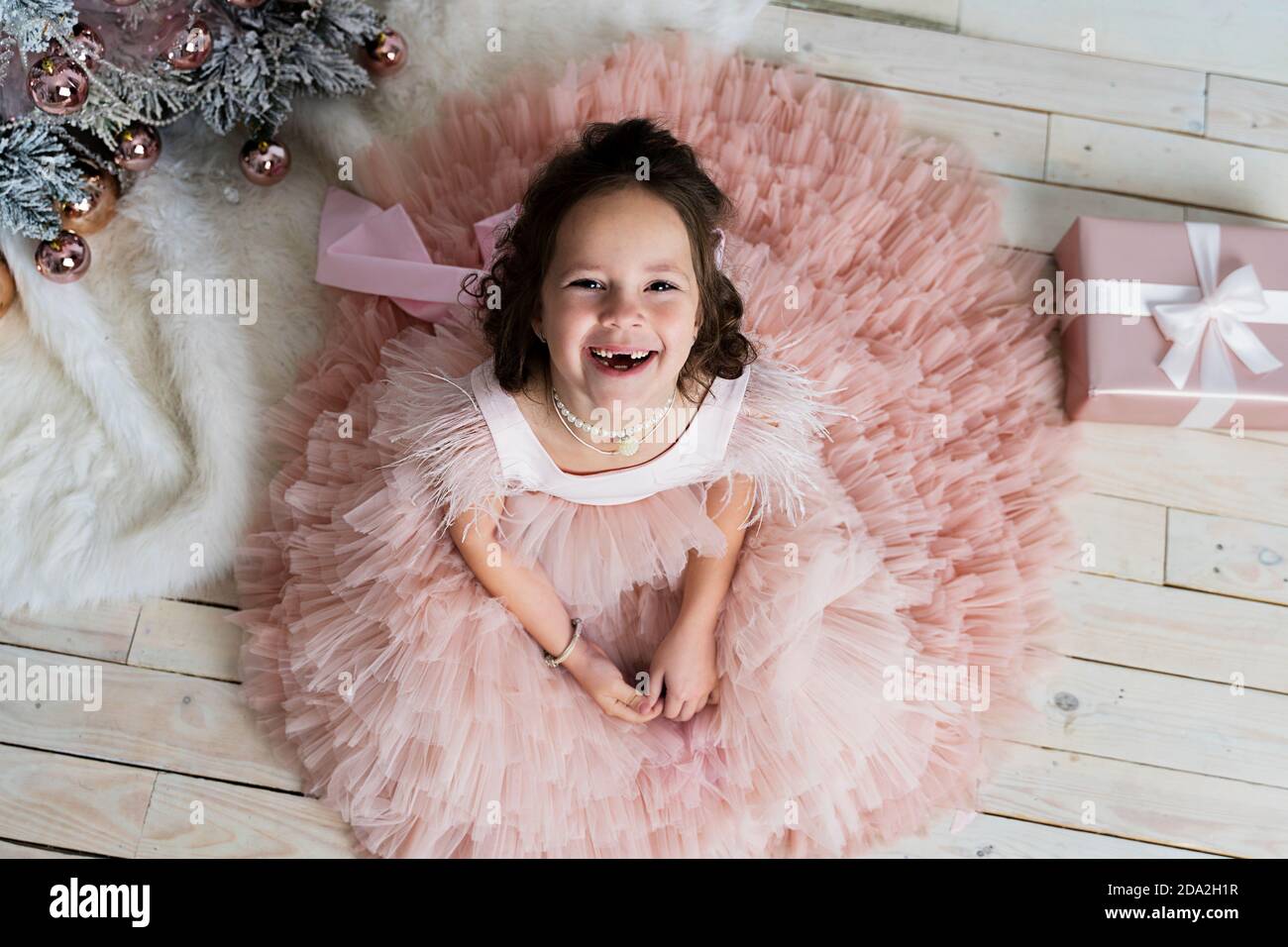 Ragazza divertente piccola in un vestito bello è felice con i regali per Natale. Foto Stock