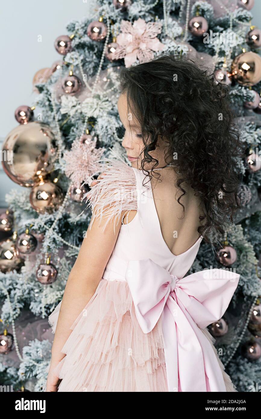 una bambina in un bel vestito si trova vicino a. Albero di Natale Foto Stock