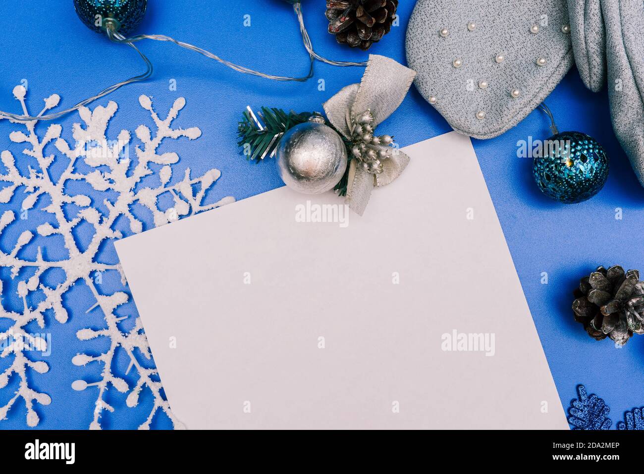 Composizione natalizia con fiocco di neve bianco, giocattolo per alberi di Natale, cono di pino e foglio bianco di carta per il testo. Sfondo blu di Natale con copia Foto Stock