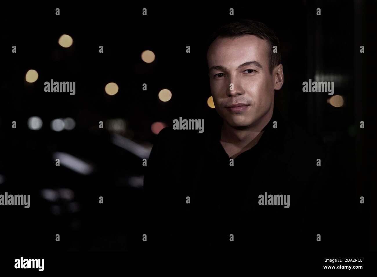 Primo piano ritratto di un bel giovane sicuro su uno sfondo nero sfocato fuori con spazio di copia, guarda la fotocamera Foto Stock