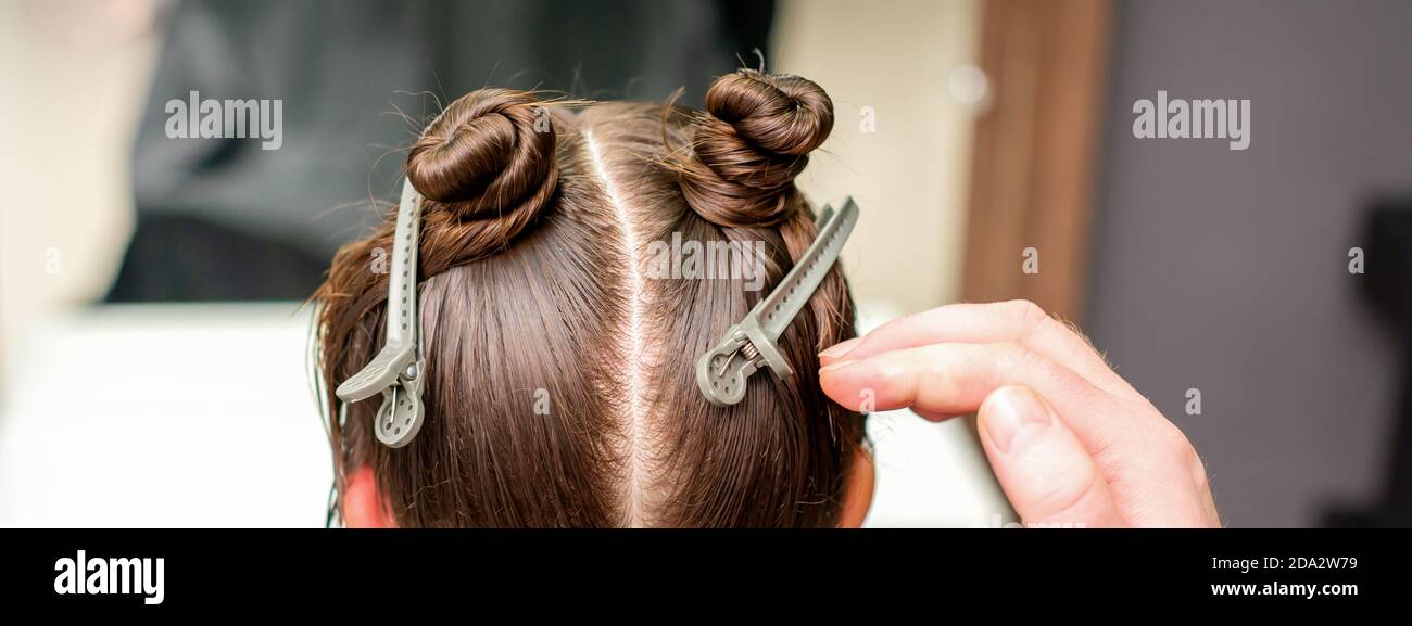 Vista posteriore della mano del parrucchiere che fa taglio di capelli di giovani donna con capelli clip sui capelli in parrucchiere Foto Stock