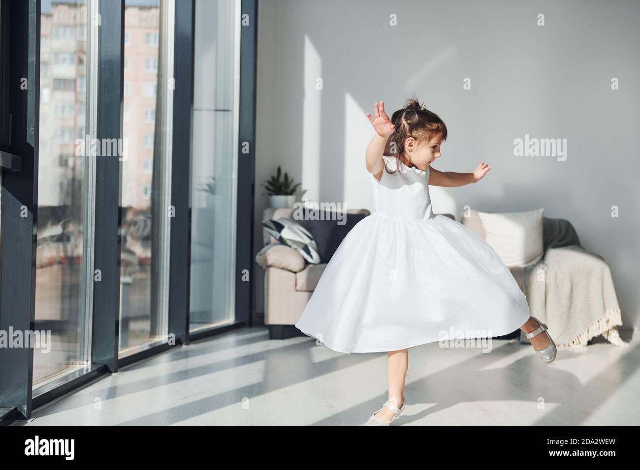 Carina bambina in abito bianco danzante all'interno in camera da letto da solo Foto Stock