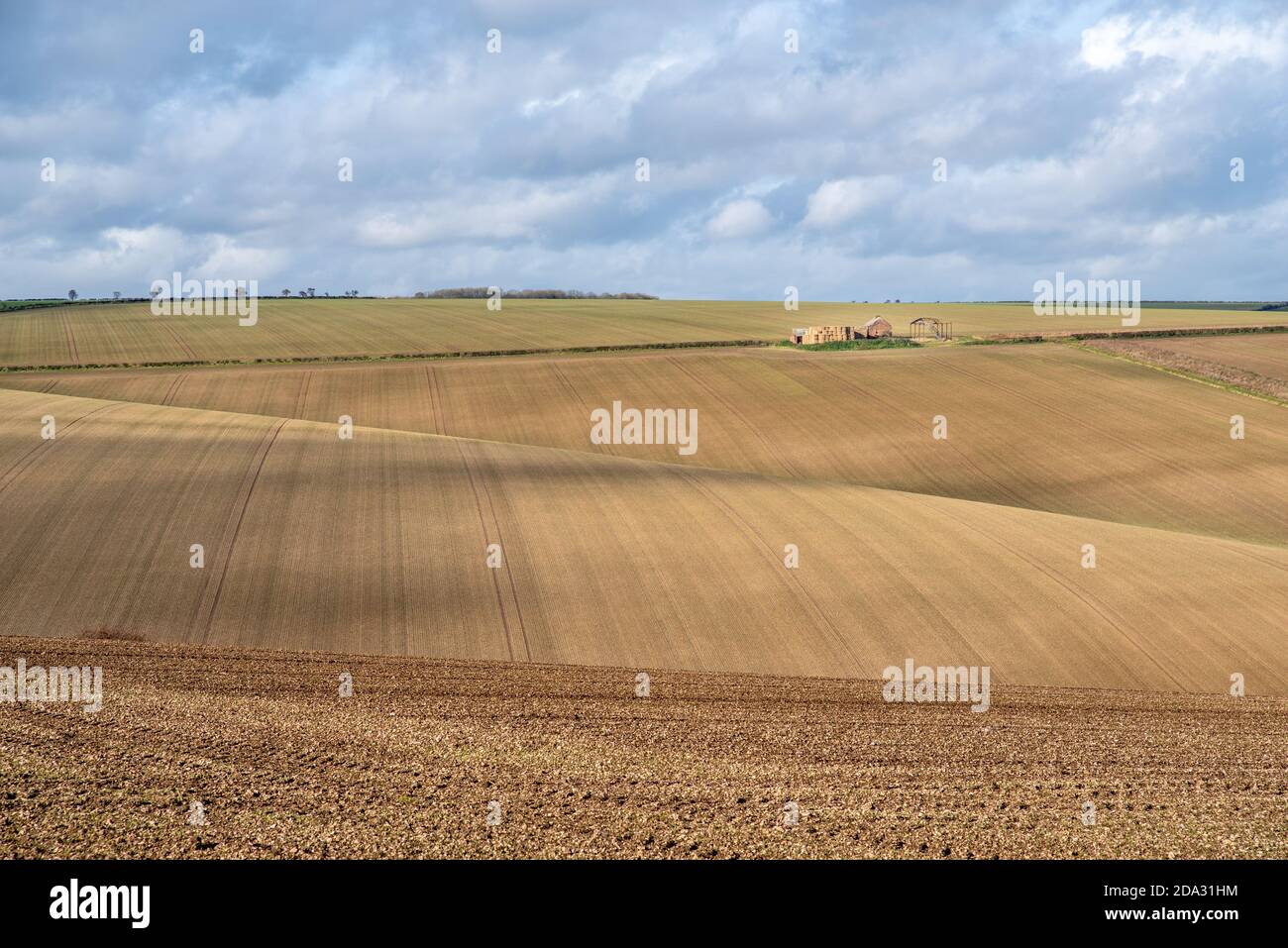 Vista di una fattoria deralict su campi ondulati arati a strisce in una giornata di sole con cielo nuvoloso. Foto Stock