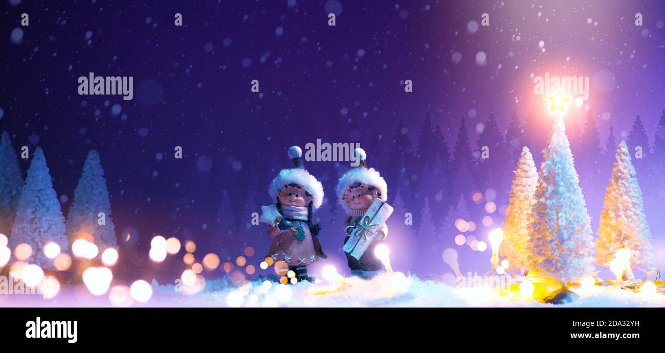 Cartolina di Natale con spazio di copia. Bambini piccoli e alberi innevati su neve morbida su sfondo rosa Foto Stock