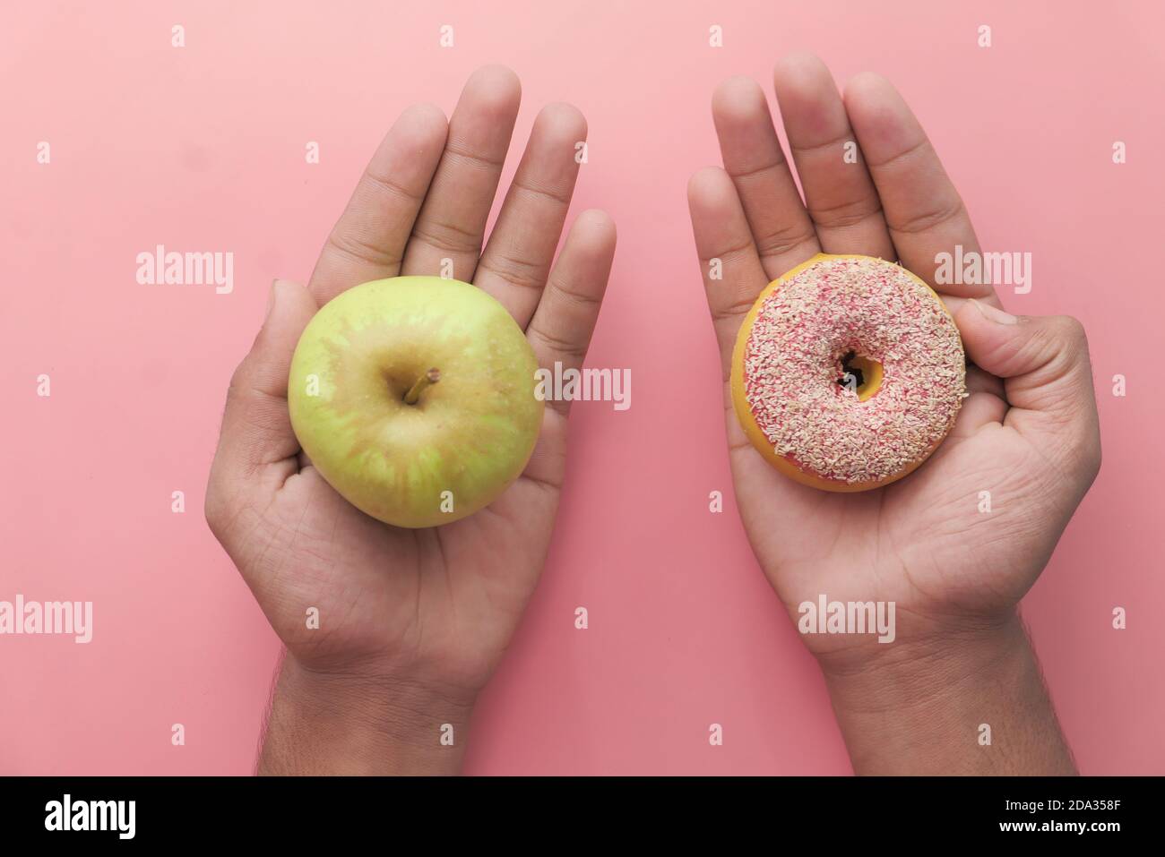 tenendo la frutta di mela e la ciambella, scelga il concetto sano di alimento. Foto Stock