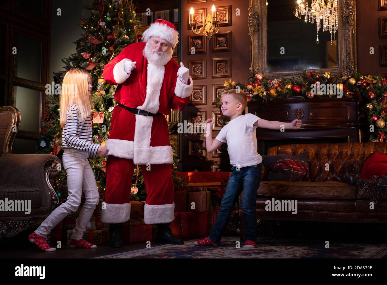 Bambini e Babbo Natale ascoltano musica e ballano a casa vicino all'albero di Natale. Sorella e fratello festivo per la famiglia che festeggia il Natale Foto Stock