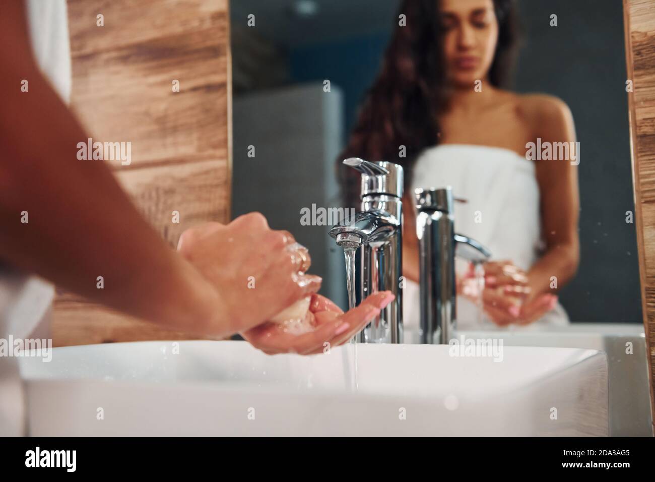 Bella brunetta in piedi in bagno vicino allo specchio e lavando le mani. Foto Stock