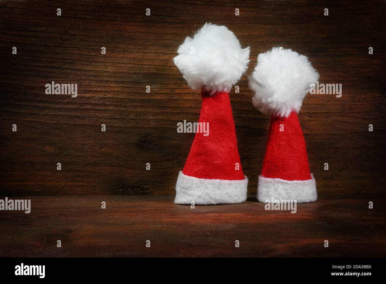 Due piccoli cappelli Babbo Natale come Avvento e decorazione di Natale su uno sfondo rustico di legno marrone scuro, spazio copia Foto Stock