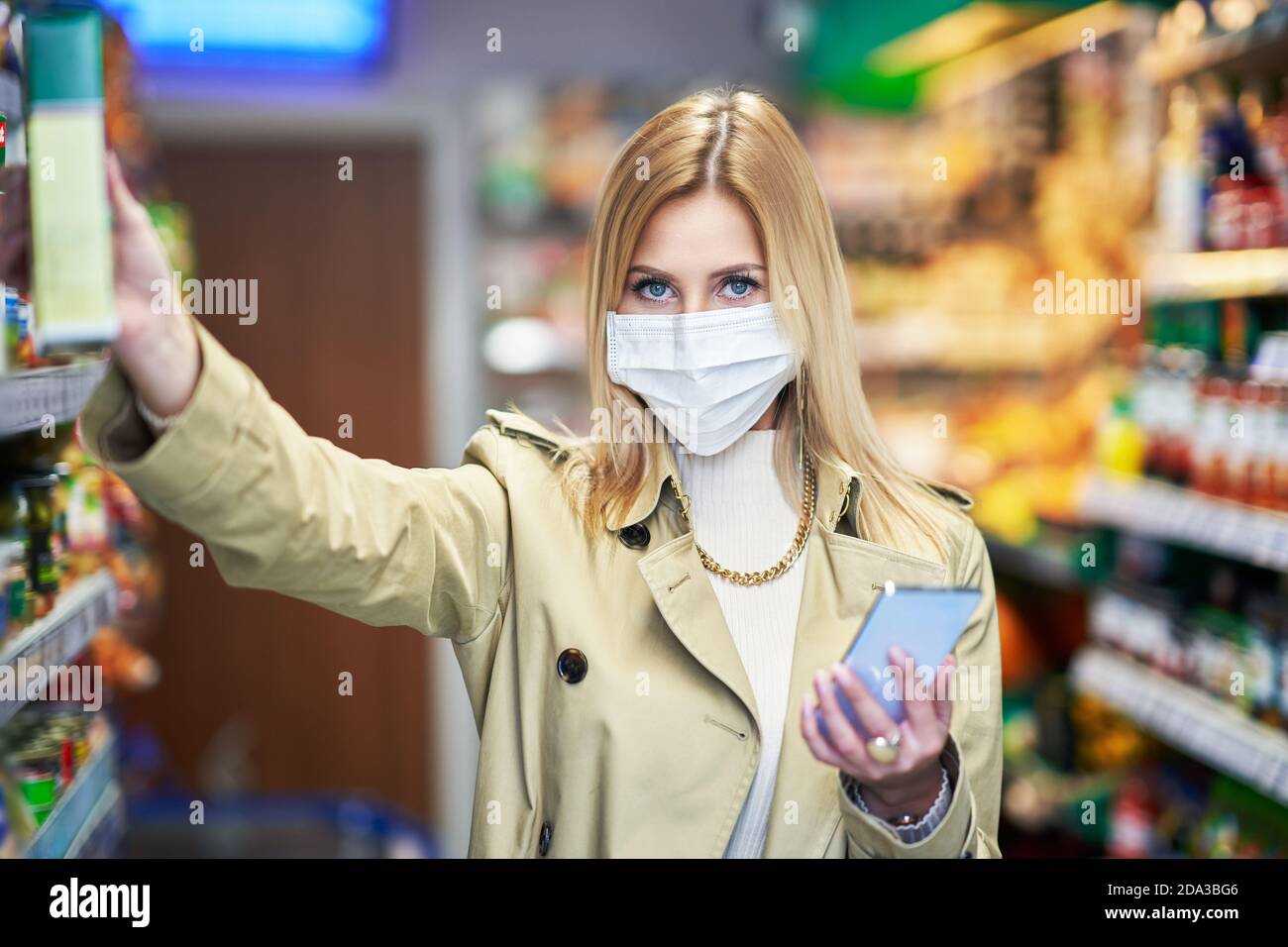 Donna adulta in maschera medica utilizzando smartphone e lo shopping per generi alimentari Foto Stock