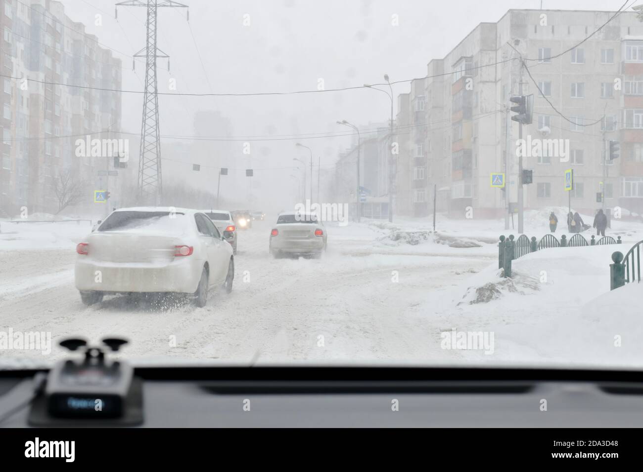 Nevicate e vento in città in inverno. Strade coperte di neve, automobili e persone congelate. Foto Stock