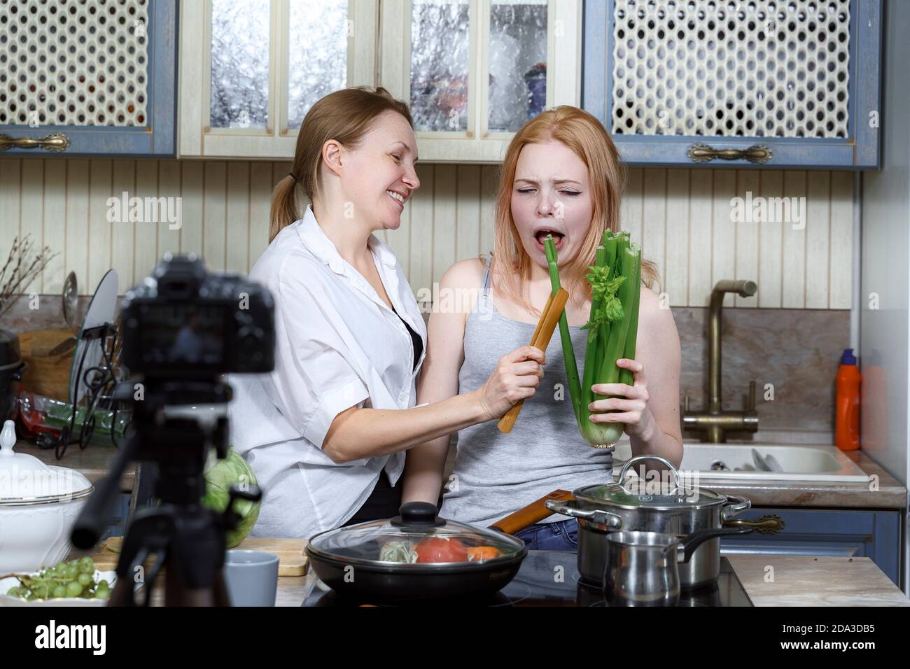 mamma e figlia stanno registrando un divertente spettacolo di cucina. vlogging alimentare. ripresa di un video pazzo su una sana alimentazione. simpatici grimaci da un morso di sedano Foto Stock