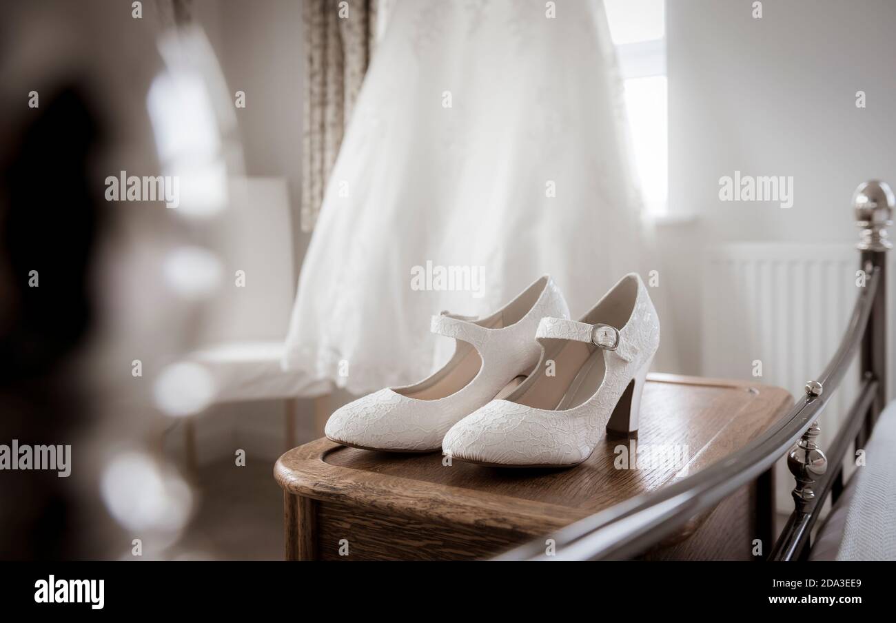 Abito da sposa appeso alla finestra di una camera da letto con scarpe in primo piano. Foto Stock