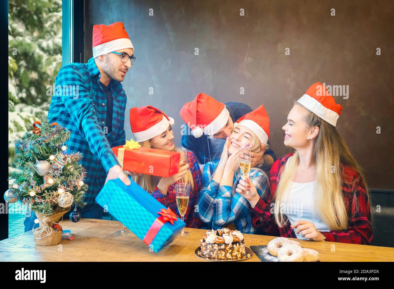 Gruppo di amici con cappelli Santa che festeggiano il Natale da condividere regali e champagne bevuto a cena a casa Foto Stock