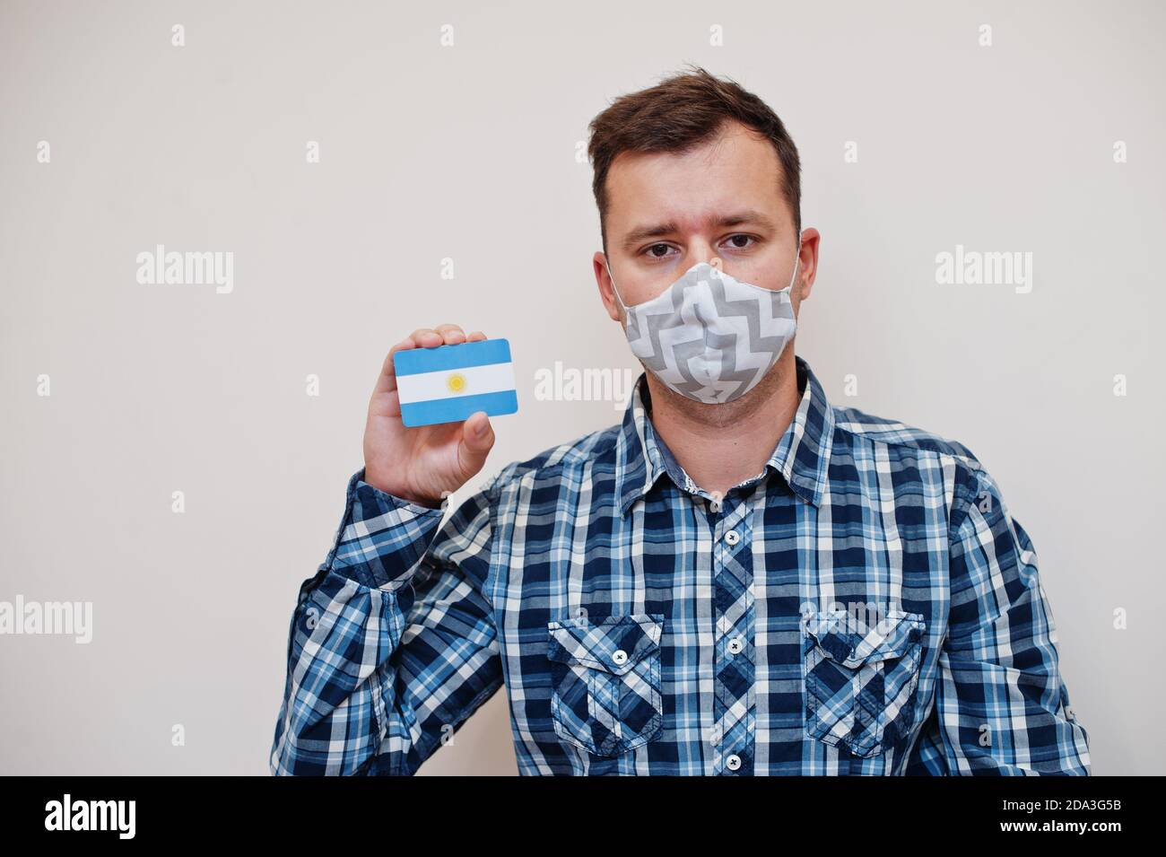 Uomo in camicia a scacchi mostra carta bandiera Argentina in mano, indossare maschera di protezione isolato su sfondo bianco. I paesi americani concetto di Coronavirus. Foto Stock