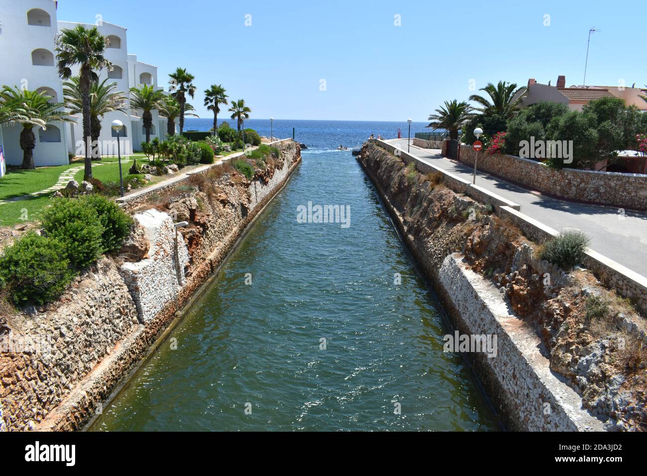 Outlet al mare in Isola di Menorca fiancheggiata da palme alberi e muri di pietra Foto Stock