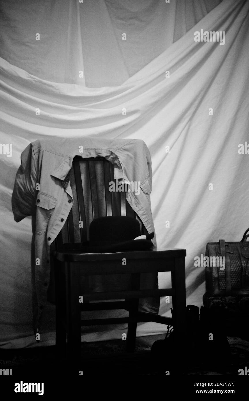 Uno studio bianco e nero ancora vita con tenda drappeggiato sfondo, borsa  in pelle, stivali, un cappello e una camicia uomo su sedia di legno Foto  stock - Alamy