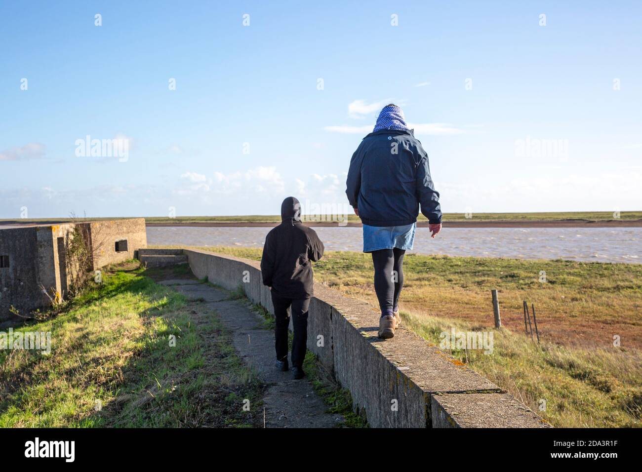 Madre e figlio adulto che camminano insieme su una parete bassa vicino al fiume ore, Suffolk, Inghilterra, Regno Unito Foto Stock