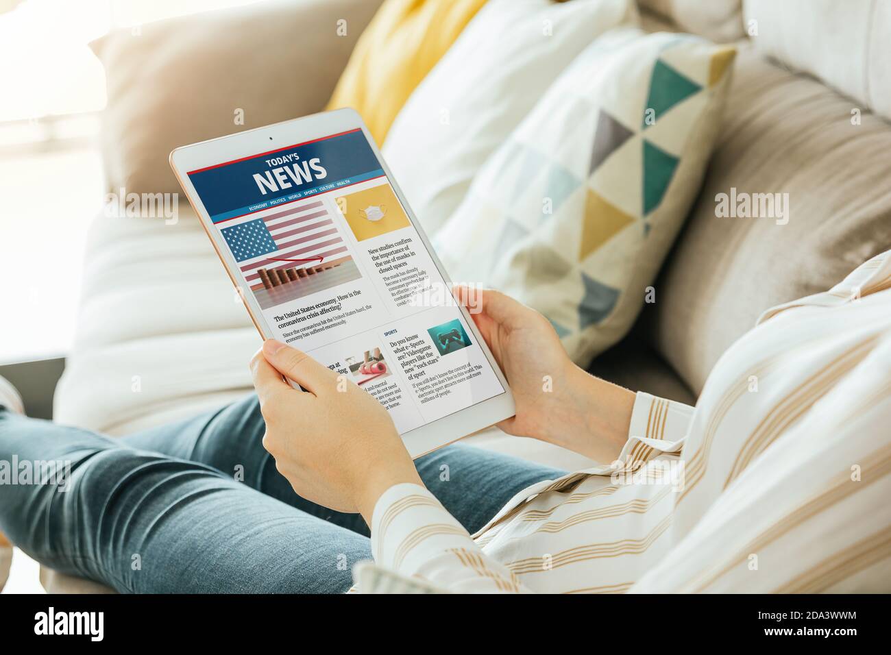Foto in stock di una donna che legge notizie online sul suo tablet dal divano. Tutti i contenuti sono composti Foto Stock