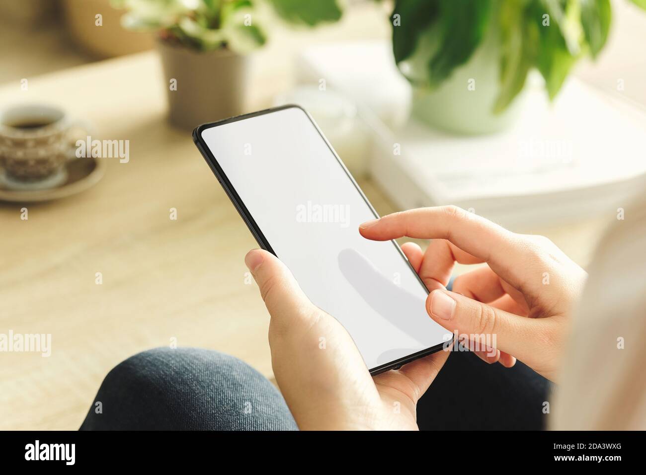 Mockup di un telefono tenuto da una donna che tocca lo schermo nel soggiorno. Schermo bianco Foto Stock