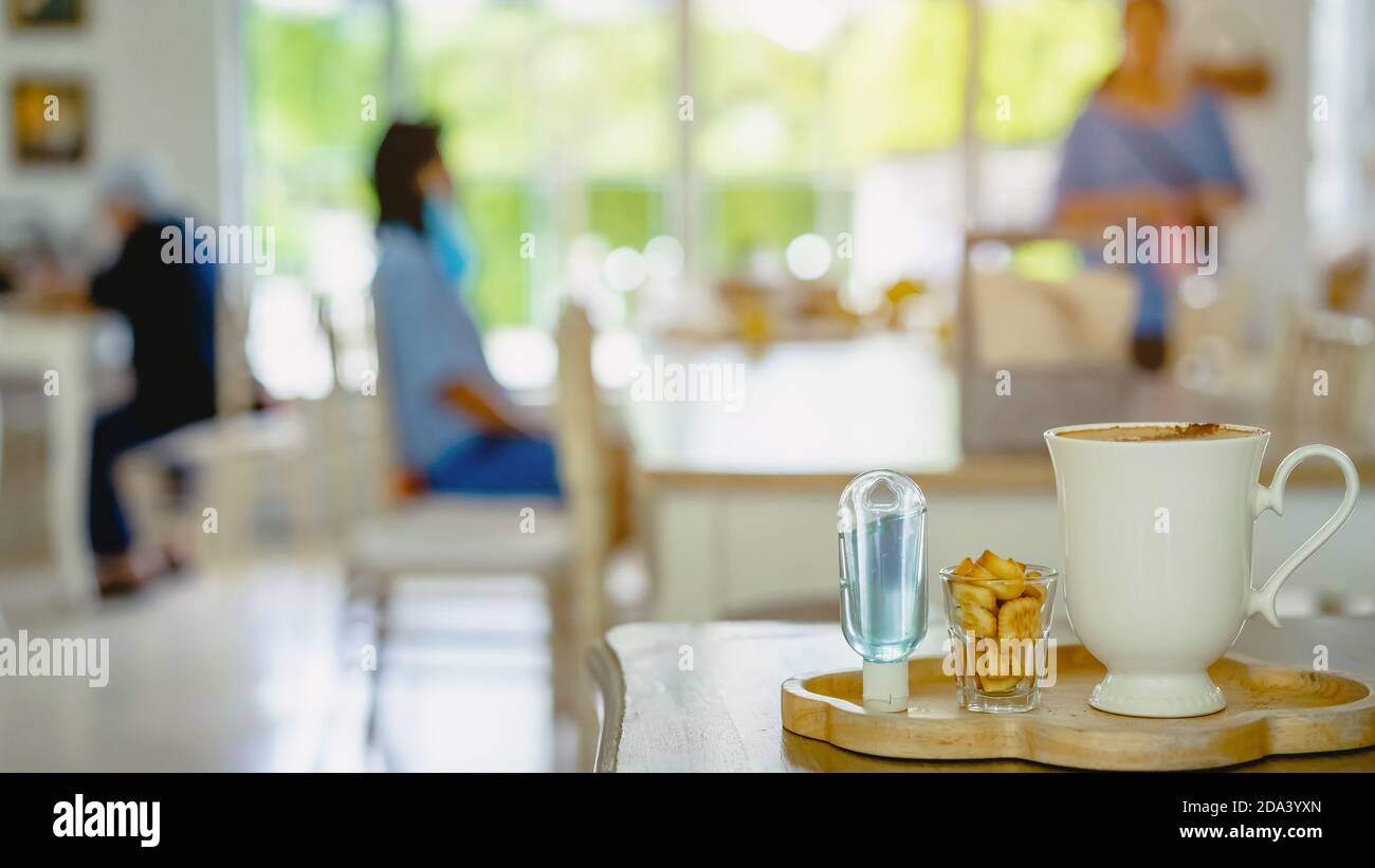 Mini flacone portatile di gel di alcol per uccidere Corona Virus (Covid-19) e. biscotti e tazza di caffè sul tavolo con immagine sfocata di una famiglia che mangia al ristorante Foto Stock