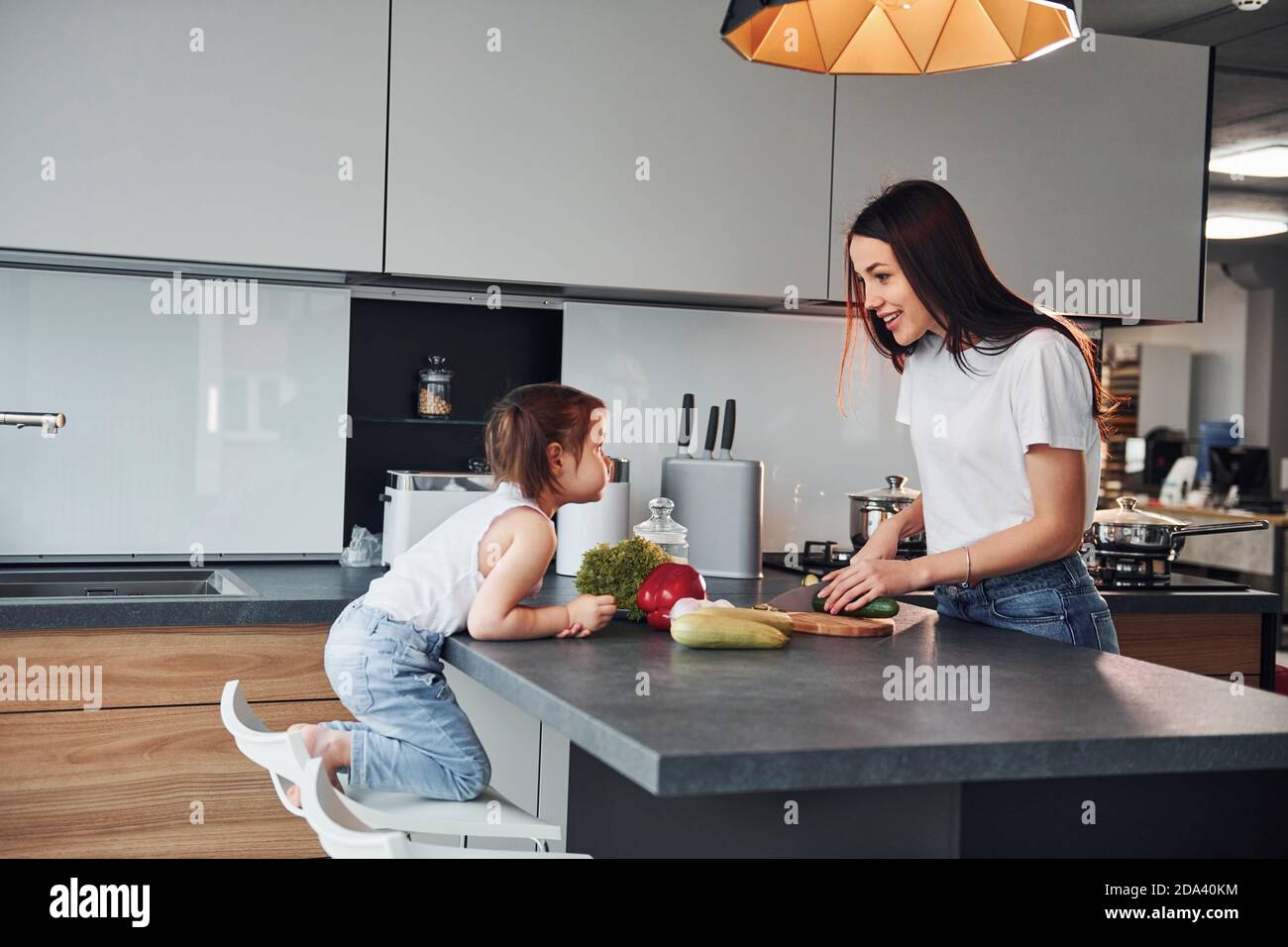 Madre con la figlia piccola che affetta le verdure all'interno in cucina Foto Stock